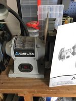 Front view of the Delta bench grinder showing the brand label, red on/off switch, and one grinding wheel.