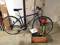 Full view of the blue Novara Corsa bicycle with air pump and owner's manual on crate in foreground.
