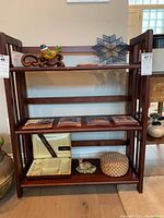 Front view of the wooden folding bookcase with three shelves, showing decorative items on the top and middle shelf.