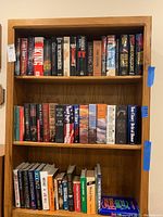 Photo of four shelves filled with hardcover and softcover fiction books by Stephen King, Tom Clancy, Ken Follett, and Dean Koontz, showing spines clearly for identification.