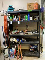 Full shelf with assorted tools, pesticide sprays, sprayers, cords, ropes, and box of garbage bags