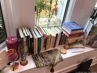 Overall view of cookbooks arranged on windowsill with decorative items including buffet caddy and glasses.