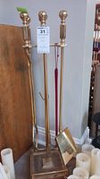 Brass fireplace tool set with stand, showing shiny finish and square base.