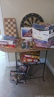 Wide shot of all games and puzzles on table and floor, showing chess board, dartboard, Monopoly and puzzle boxes.