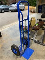 Full view of blue metal hand truck, showing frame, handles, base plate, and tires