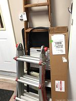 Image showing wooden ladder, metal folding stepladder with red knobs, black folding table, and boxed gutter screens next to a door.