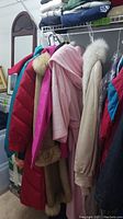 Photo showing multiple ladies coats hanging including coats with fur collars and bright colors.