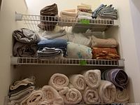 Overview of linens and towels stacked on wire closet shelves showing folded sheets and rolled towels