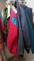 Front and side view of six men's outerwear items hanging on a rack, including coats, jackets and a vest