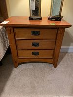 Front view of wooden nightstand with three drawers and metal handles