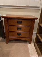 Front view of wooden nightstand showing three drawers with metal handles, slightly flared legs.