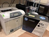 Photo shows beige HP LaserJet 4250 laser printer next to a black and white HP box containing the 42X Q5942X toner cartridge.