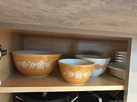 Three mixing bowls on shelf: two golden yellow with white floral design and one white with gold floral pattern