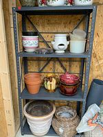 Front view of the four-shelf metal shelving unit containing various ceramic and plastic pots and a woven basket underneath.