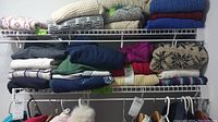 Folded sweaters in various colors and knit patterns on wire shelves showing different textures and patterns.