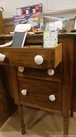 Front view of walnut sewing table with open top drawer showing white knobs and items on tabletop.
