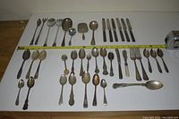 Full layout of 39 assorted cutlery pieces on white surface with measuring tape