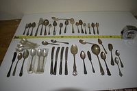 Top-down view of assorted cutlery laid out with a measuring tape for scale, showing variety in size and style