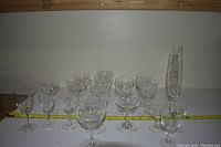 Photo showing assortment of 20 clear glassware items including wine glasses, cocktail glasses and champagne flutes, arranged with measuring tape for size reference.