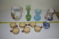 Wide shot showing all items including pitchers, glass vases, and cups arranged in a line.