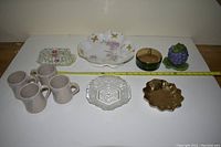 Full view of six assorted decorative dishes and figurine arranged on a flat surface with measuring tape for scale.