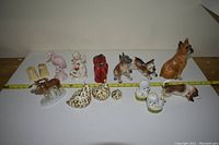 All assorted ceramic and porcelain figurines, including dog, bird, pig, pepper shakers, and character figures displayed against a plain background with measuring tape.