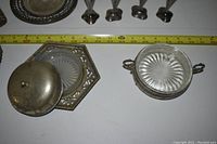 Two silver dishes with decorated glass inserts, one round with lid and handles, the other hexagonal with openwork border, shown with ruler for size.