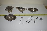 Overview photo showing all silver items including two pierced trays, sauce boat, sugar bowl with lid, tongs and spoon.