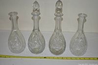 Four clear crystal decanters displayed side-by-side, two have stoppers, two do not. Each has carved floral/star patterns.