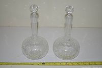 Full view of both crystal decanters with stoppers placed side by side on a flat surface with measuring tape showing size scale.