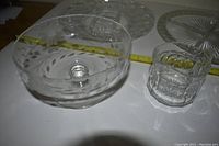 Clear glass bowl with leaf or floral cut pattern and small handled starburst bowl beside it on table with measuring tape.