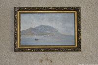 Front view of Leslie Skelton oil painting featuring mountain and lake scene in decorative gold and brown frame on carpet.
