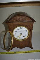 Front view of the vintage mantel clock showing the arched wooden case, decorative inlays, clock face with glass door open, and gold clock hands.