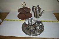 Full shot of all items including the metal serving tray with bowls and pitcher, wooden two-tier tray, and metal coffee pot on a white surface with measuring tape.