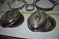 Photo showing five silver serving pieces together: two oval dishes with lids, two trays with handles, and one round item with side handles. Items show tarnish.