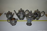 Five piece silver-plated tea set with tarnish, floral embossed designs, various handles and lids