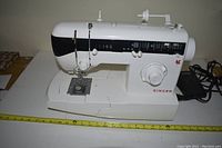 Front and left side view of white Singer sewing machine Model 2732 with multiple stitch options and foot pedal.