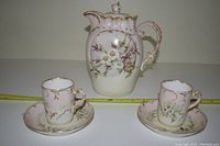 Front and side view of teapot, one cup and saucer, showing floral and gold details against pink background.