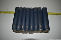 Nine volumes of Shakespeare's works with dark blue spines and gilt text, some damage on top edges, aligned side by side with measuring tape showing size.