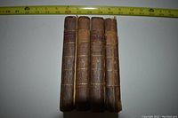 Four small leather-bound books spines facing viewer, gilt bands and red spine labels reading "WORLD", ruler above indicates size