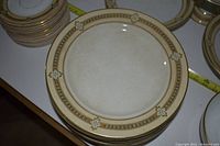 Close-up image of stacked large plates showing beige and gold floral border, minor usage signs