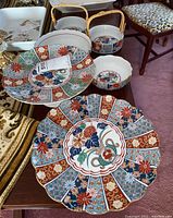 Overview of five Japanese ceramic items on table with floral and geometric decoration in red, blue, green, and gold, including scalloped cake plate and bowls with handles.