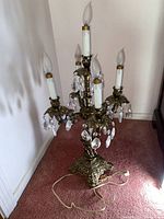 Full view of brass candelabra style lamp showing five candle-shaped bulbs and crystal pendants, ornate brass base and arms, on pink carpet.