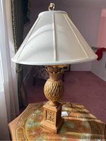 Full image of the brass pineapple lamp with white shade on a decorative table near a window.