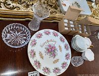 Photo showing crystal vase, Happy Birthday plate, boxed porcelain napkin holders, white cups, and crystal toothpick holder on wooden surface.