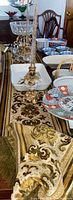 Photo showing one brass ornate candle holder with a tall gold-fleck holiday candle, Shafford Chinese Garden china pieces including casserole dish and bowls on a table with decorative table runners.