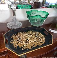 Photo of crystal decanter, green art glass bowl, and black tole painted tray arranged on wooden surface with mirror background.