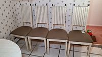 Front view of four identical dining chairs lined up against a wall with floral wallpaper, showing brown upholstered seats and light-colored laminate composite frames with tall slatted backs.