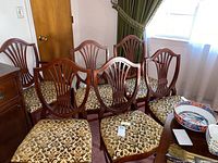 Six vintage wooden dining chairs arranged, showing shield backs and patterned seats. Four armless chairs and two armchairs visible.