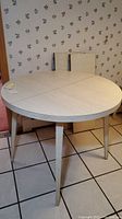 Round laminate dining table shown with leaves stored upright against wall and table in unextended form.